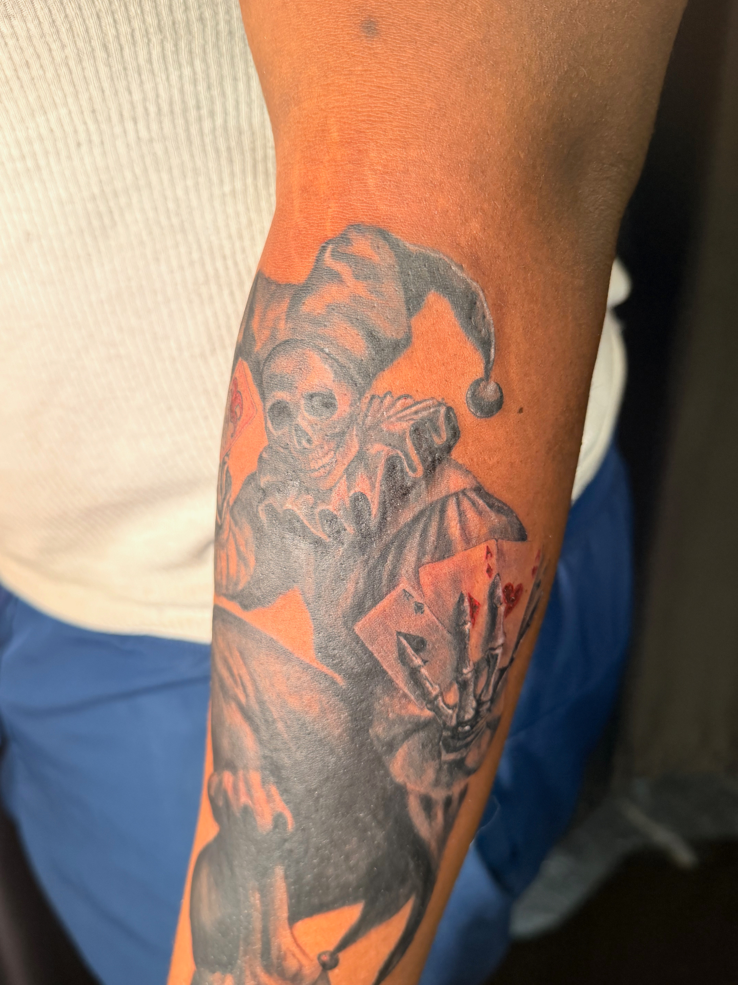 Black and grey grim jester with playing cards forearm tattoo