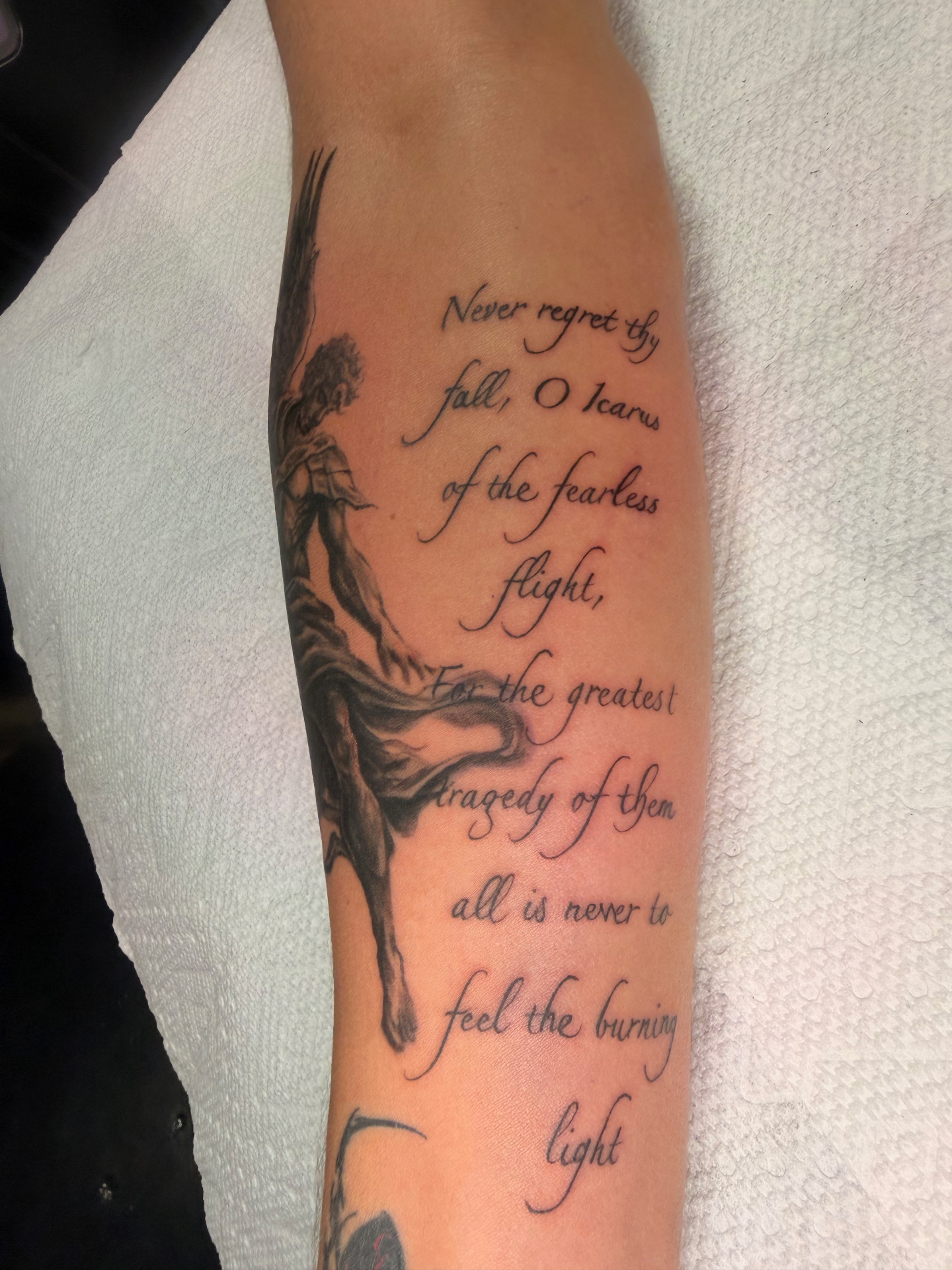 Black and grey Icarus forearm tattoo with poetic script quote