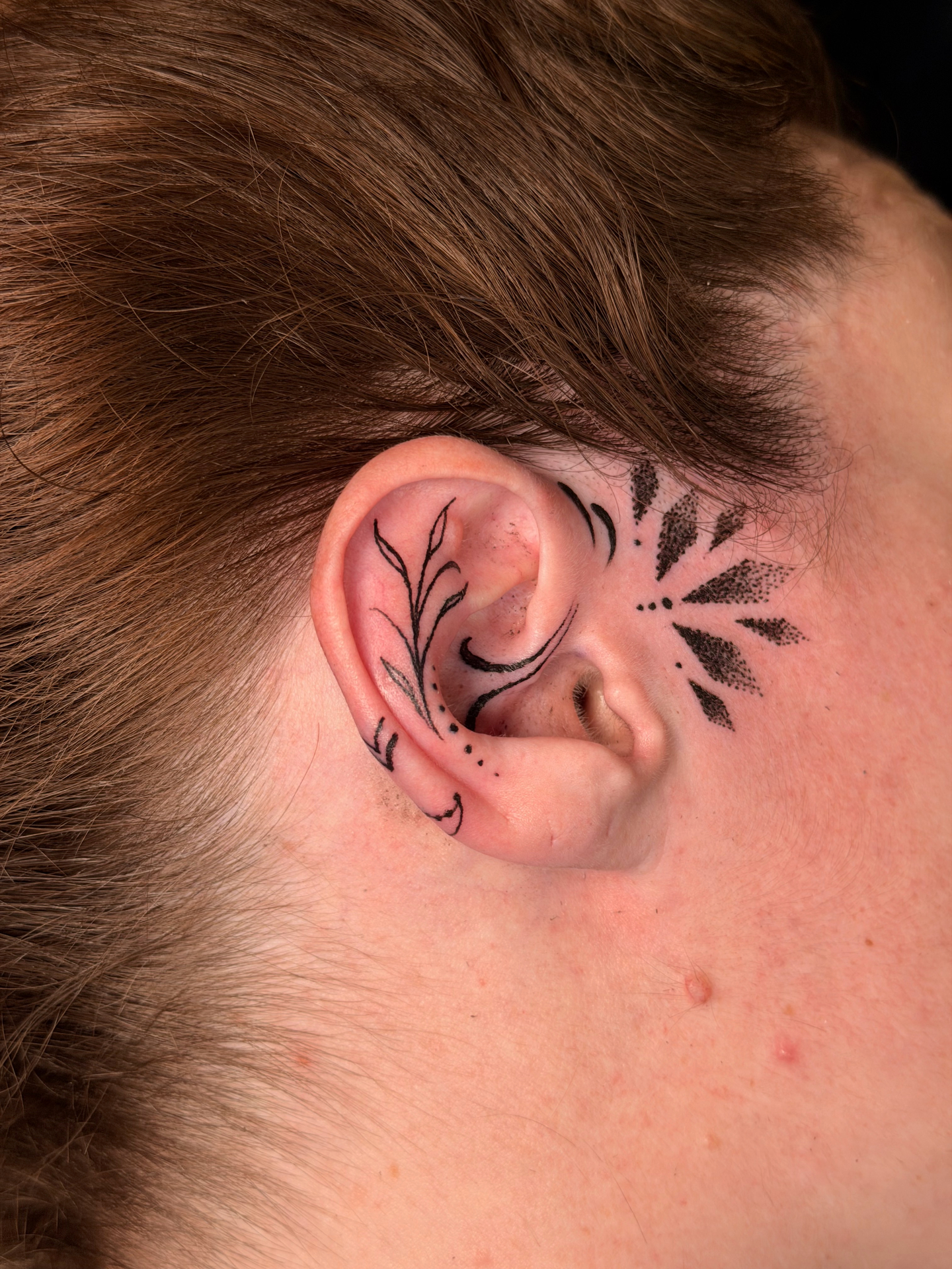Fine line ornamental ear tattoo with floral linework and dotwork sunburst