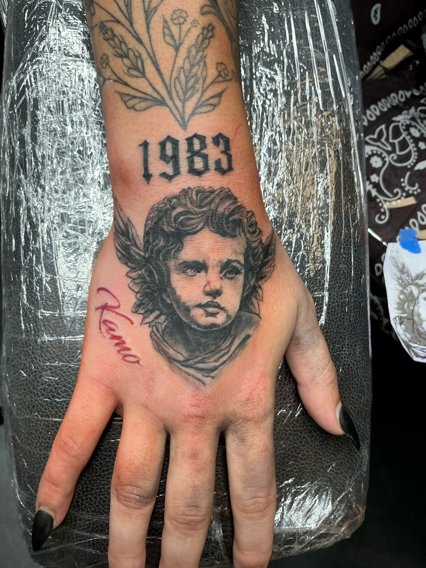 Black and grey portrait hand tattoo with 1983 gothic lettering and Reno script