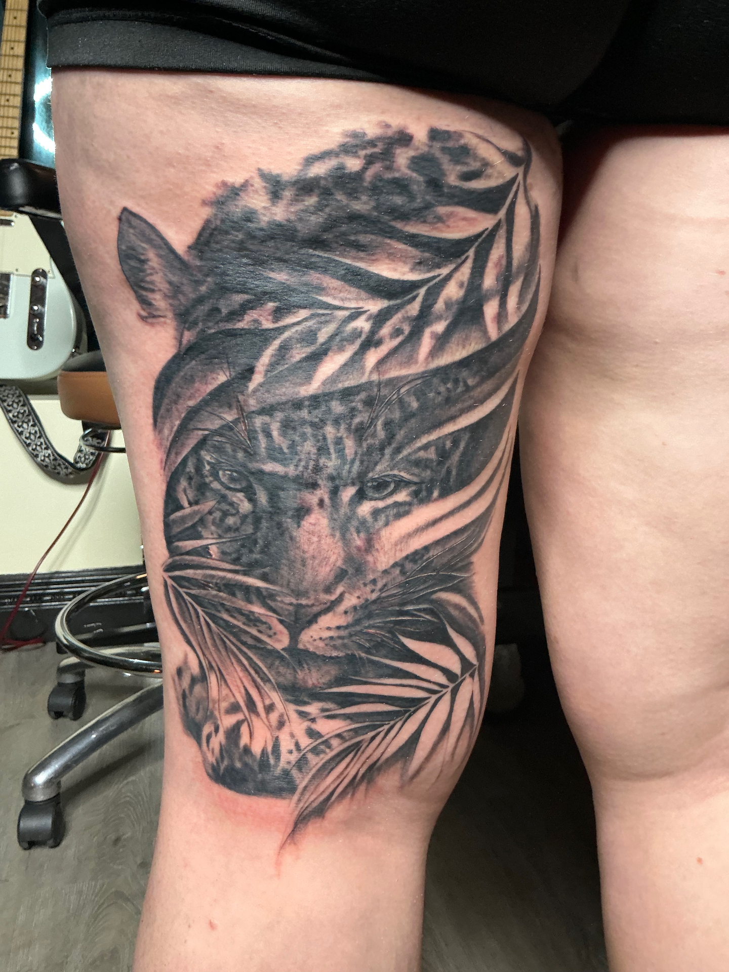 Black and grey tiger portrait with layered foliage thigh tattoo