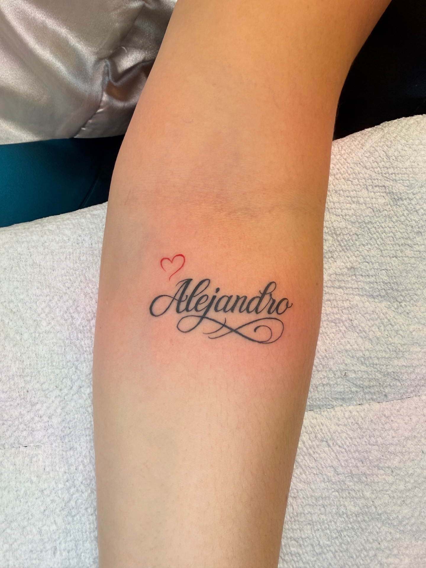 Alejandro script lettering tattoo with red heart