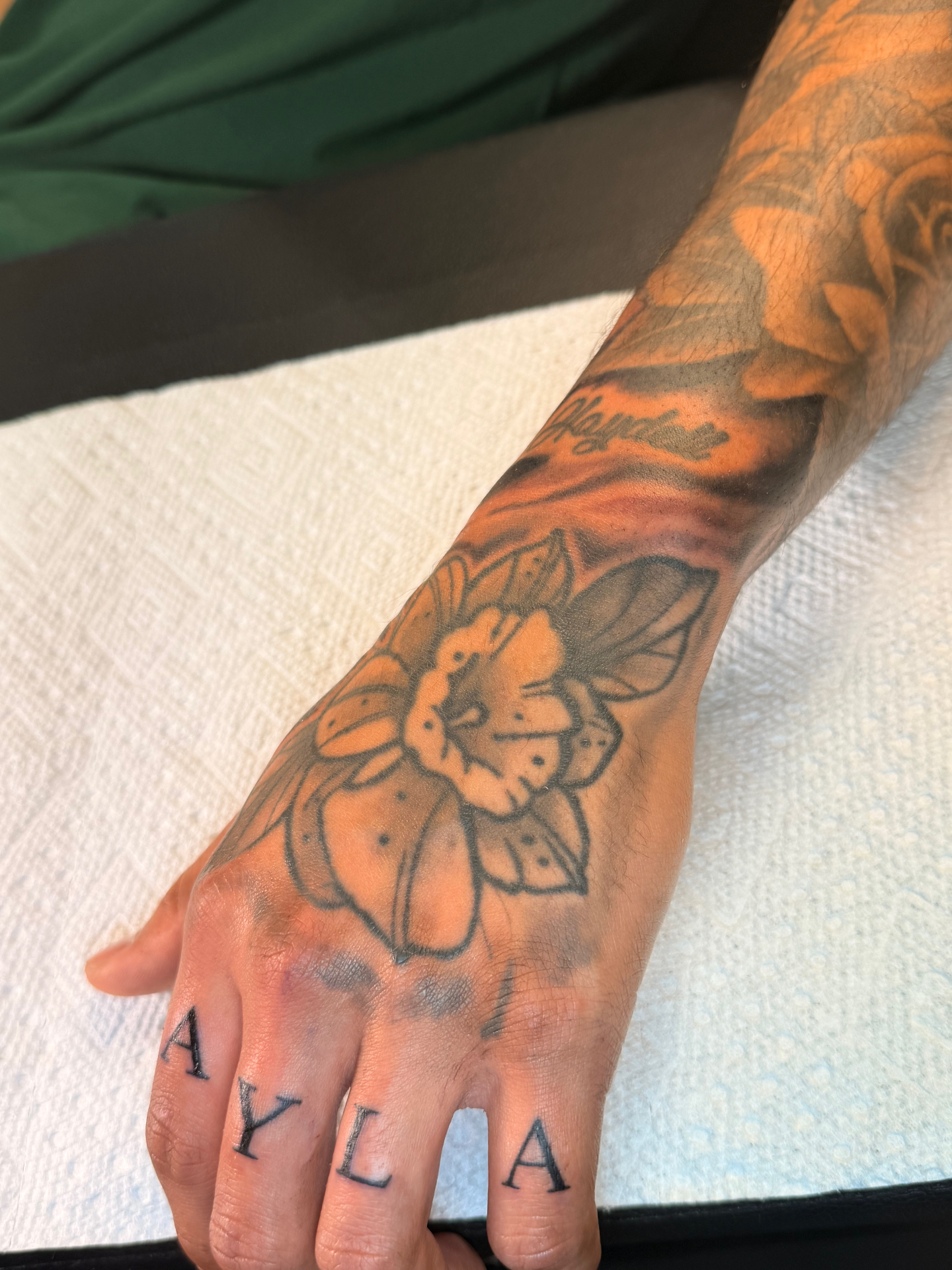 Black and grey traditional daffodil hand tattoo with Ayla knuckle lettering