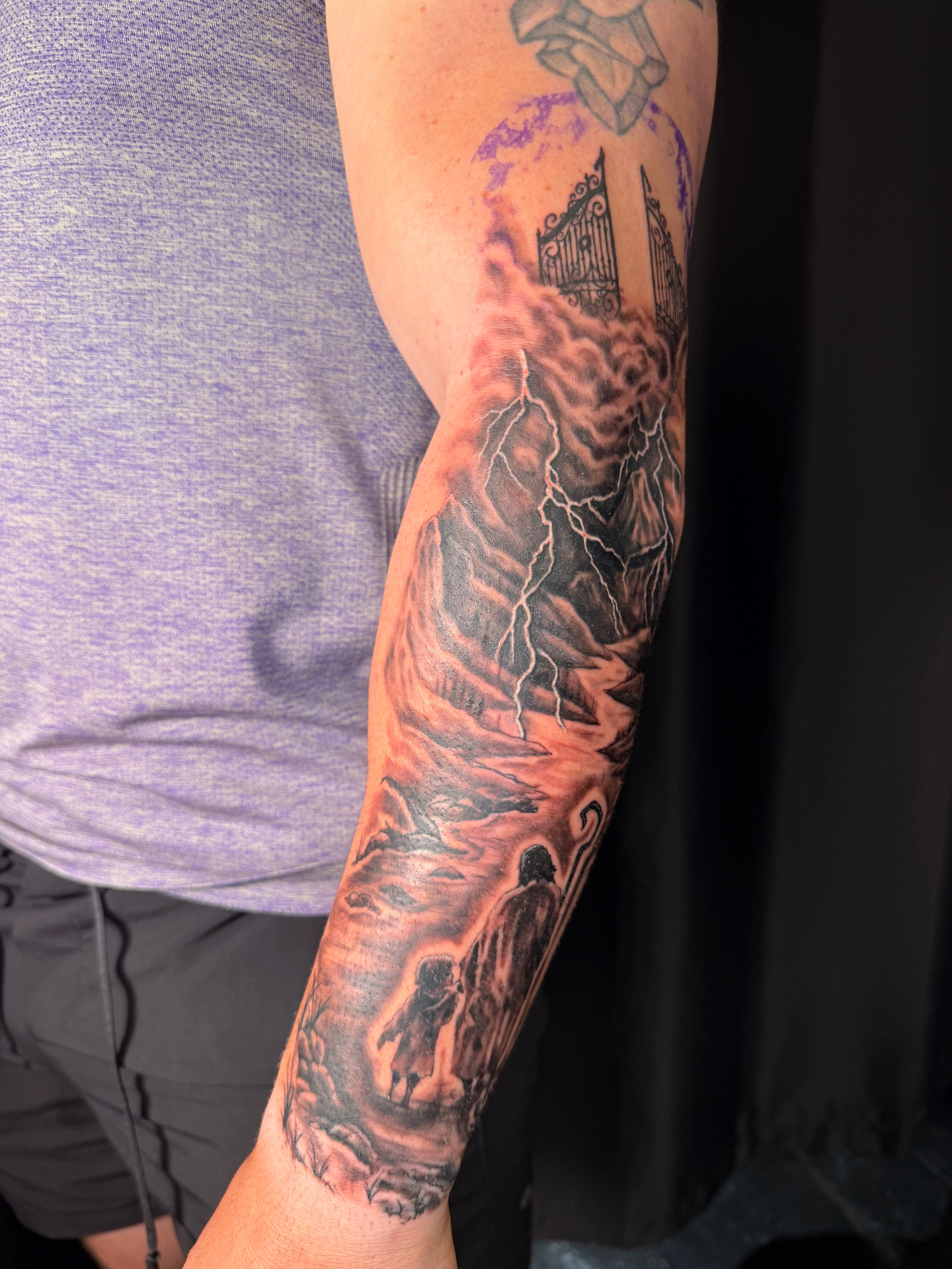 Black and grey realism sleeve tattoo with shepherd, stormy mountains, lightning and gates of heaven