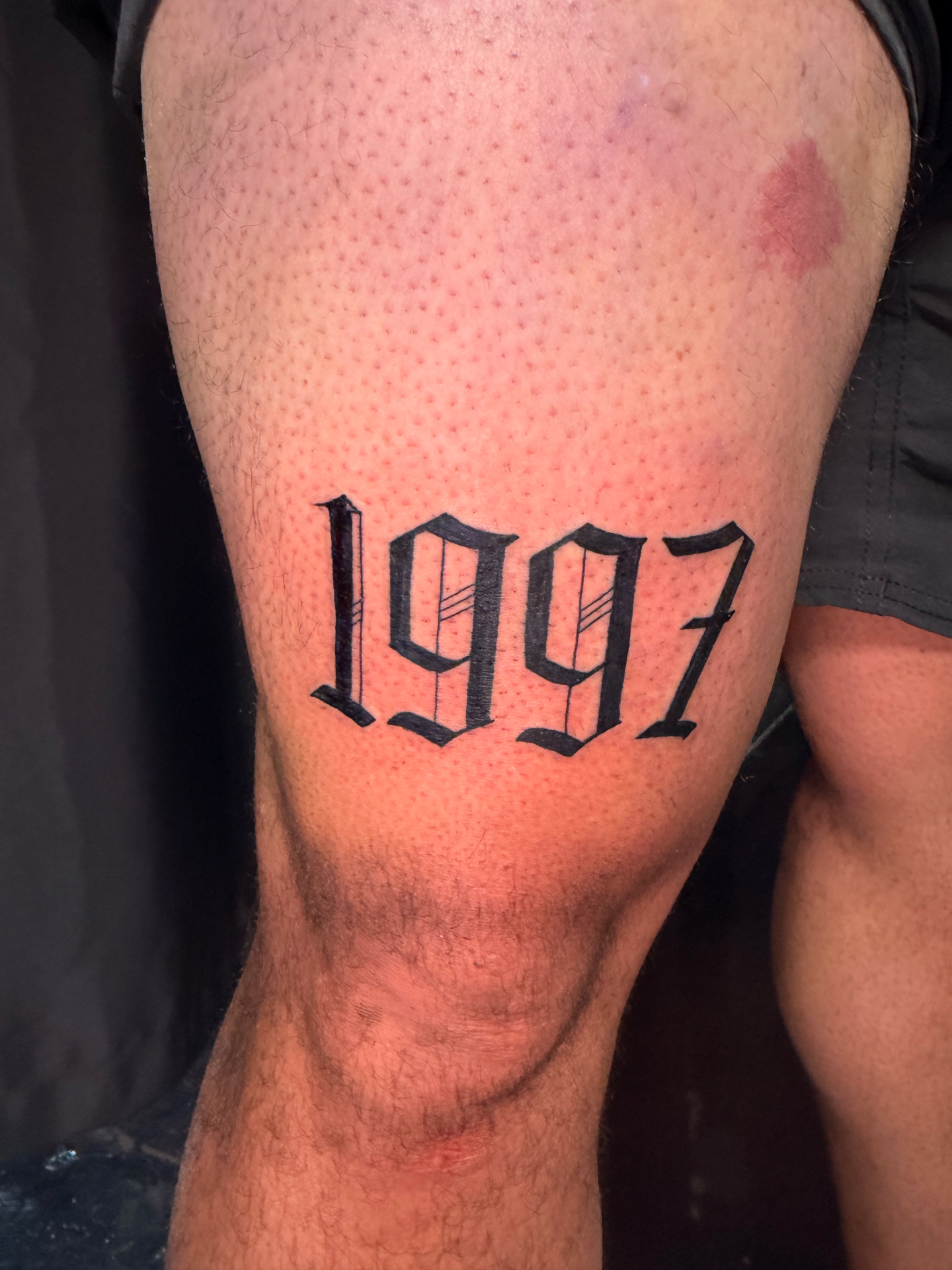 Bold black 1997 gothic lettering thigh tattoo