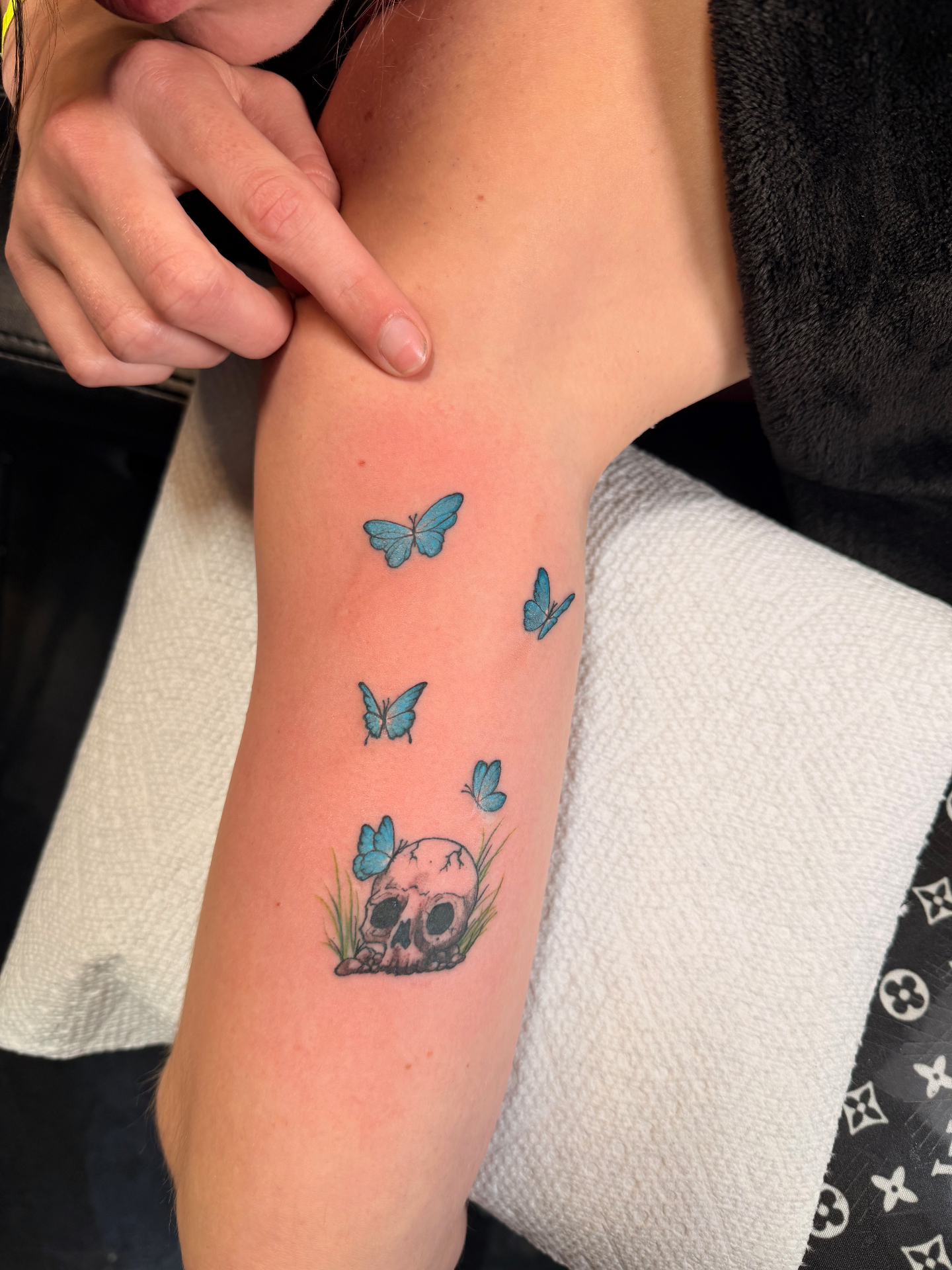 Skull tattoo with blue butterflies and grass on forearm