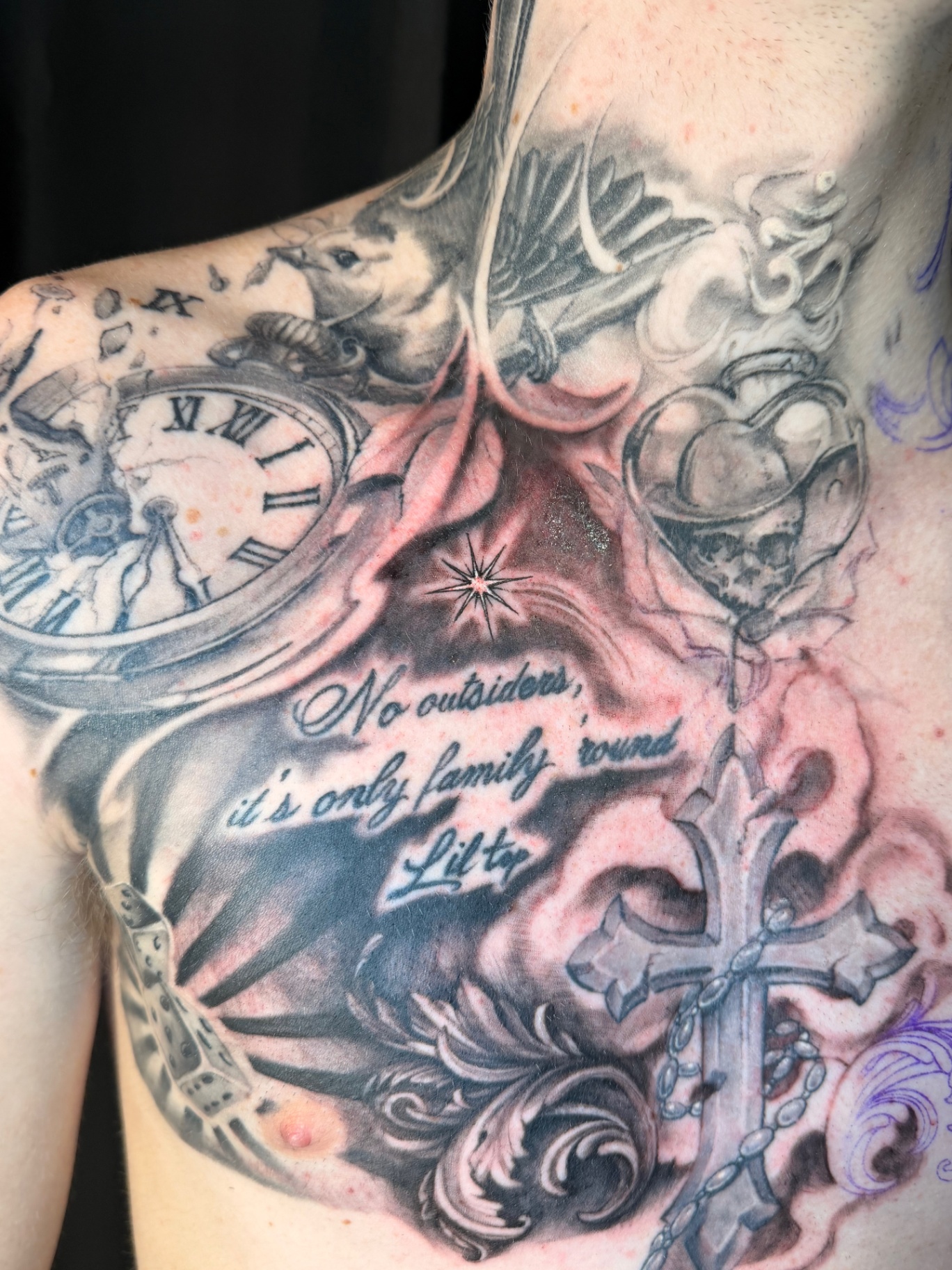 Black and grey chest tattoo detail with pocket watch, starburst, cross and family script